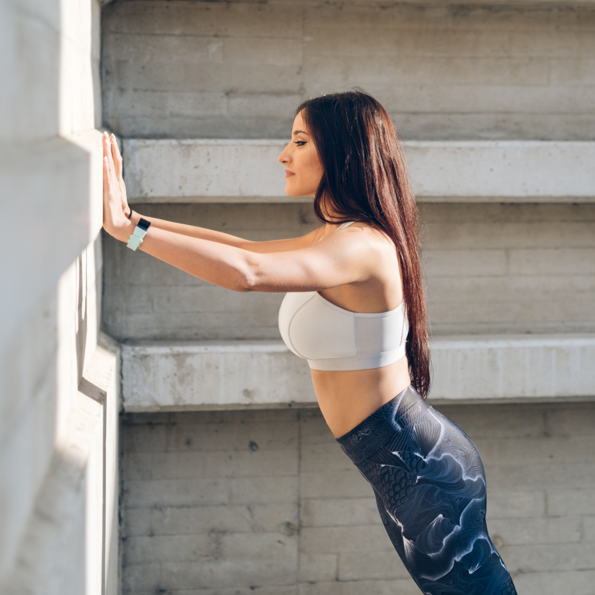 woman doing wall push ups long brown hair white top blue leggings