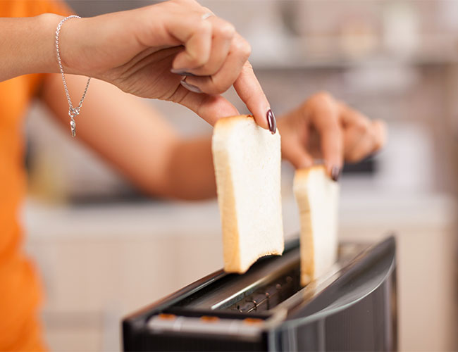 woman with manicured nails placing two slices of white bread in toaster