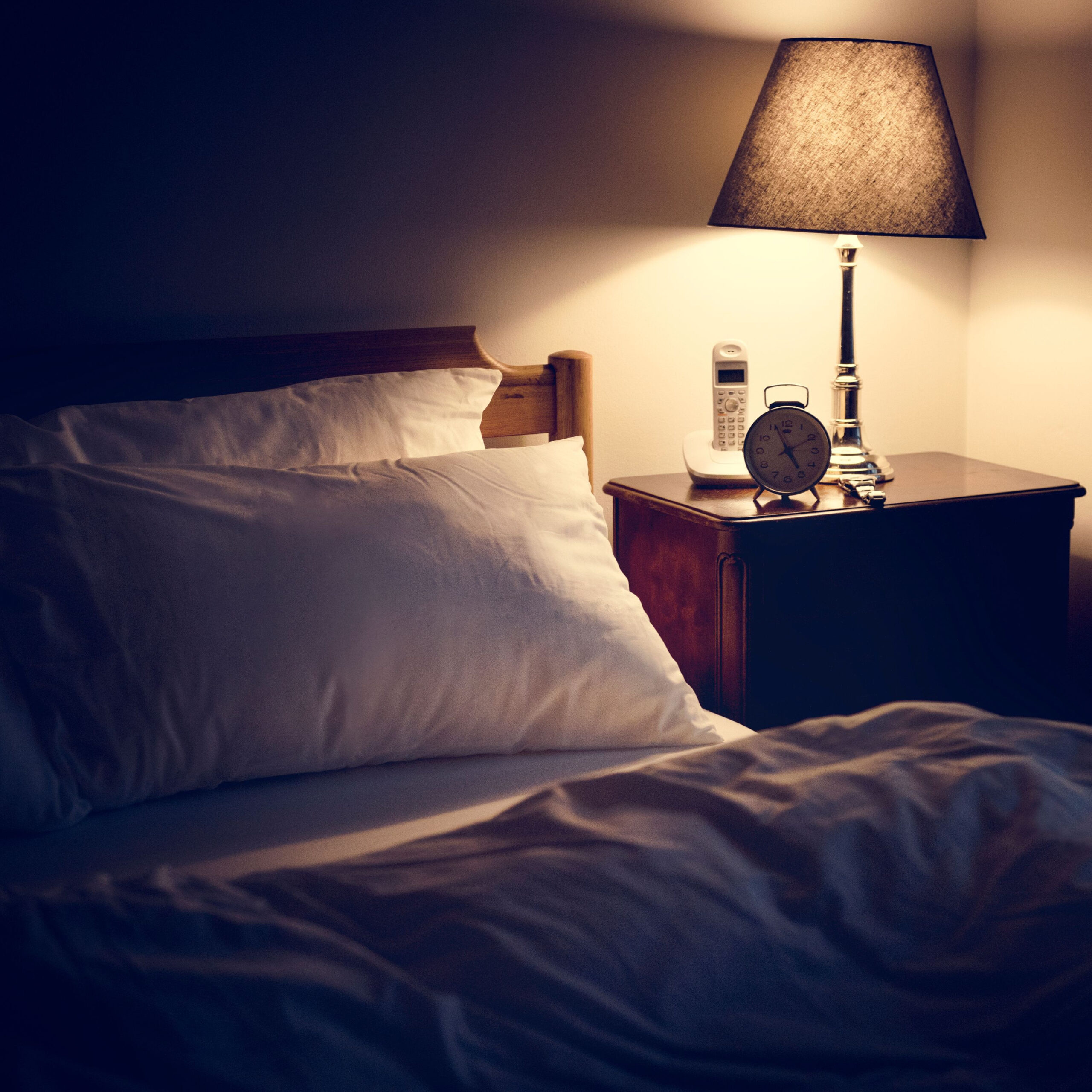 bed at night with an alarm clock and lamp on bedside table