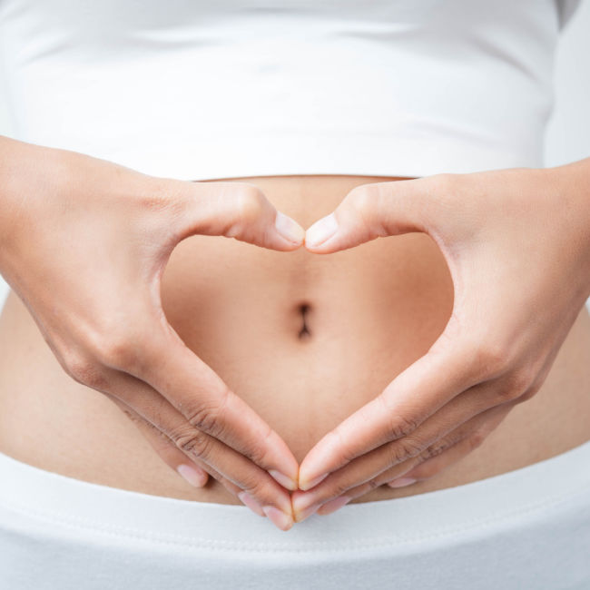woman holding hands in a heart over her belly button