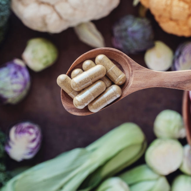 wooden spoon of fiber supplements above display of high-fiber veggies