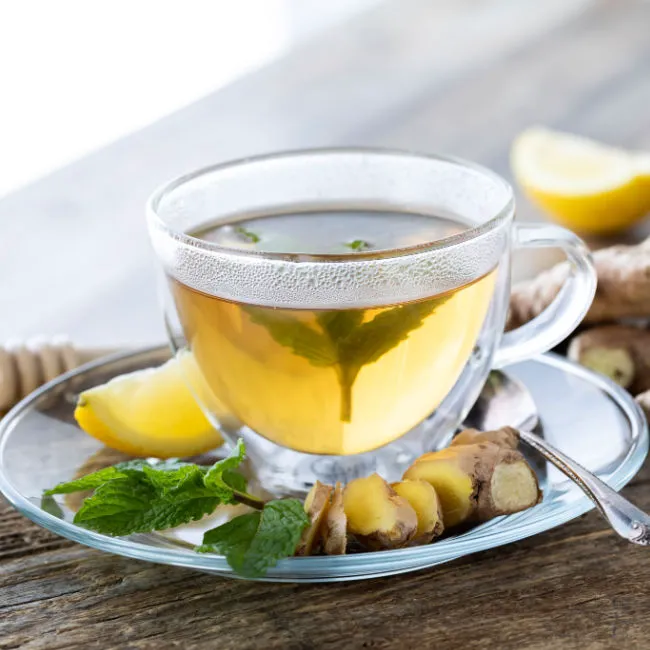 glass cup of ginger tea on saucer with lemon wedge and sliced ginger