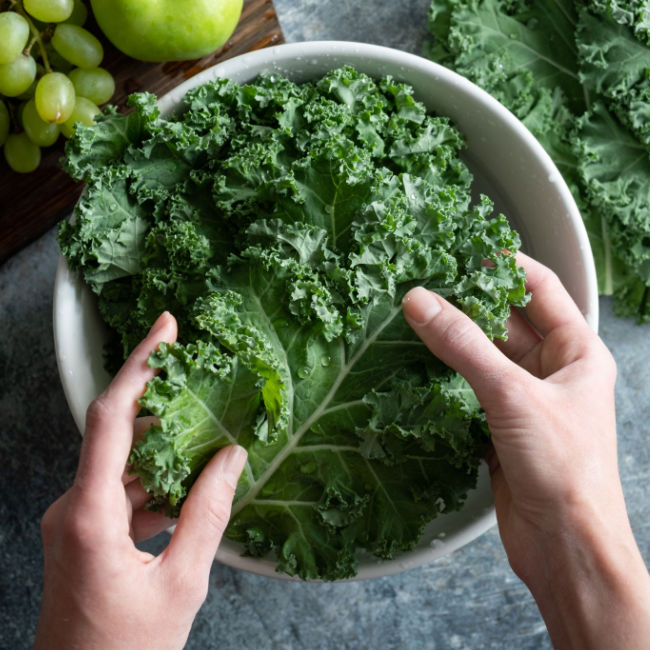 hands massaging kale in white bowl on kitchen counter
