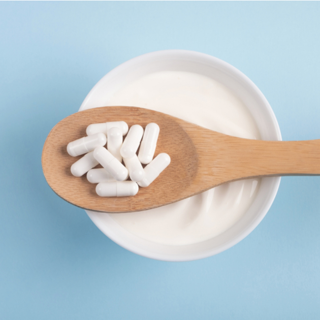 wooden spoon filled with probiotic supplements resting on top of small bowl of yogurt