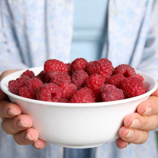 woman holding bowl of raspberries