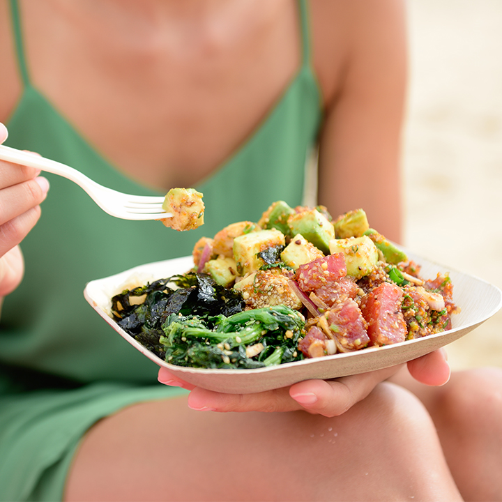 woman eating poke bowl salad on beach