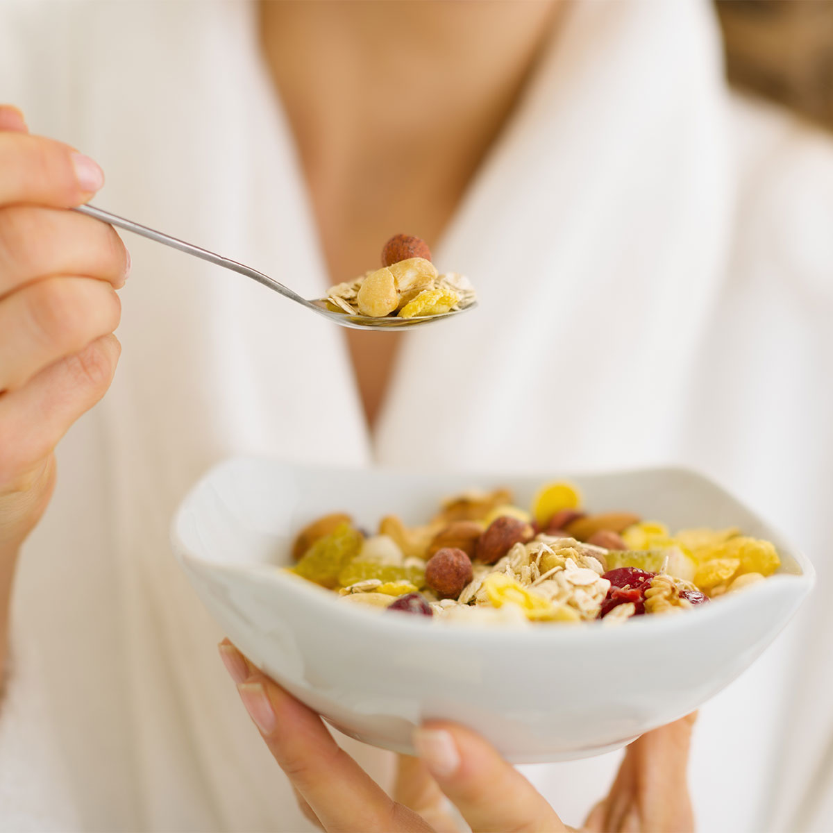 woman in robe eating oatmeal topped with dried fruit