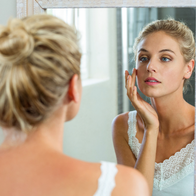 woman examining face in mirror