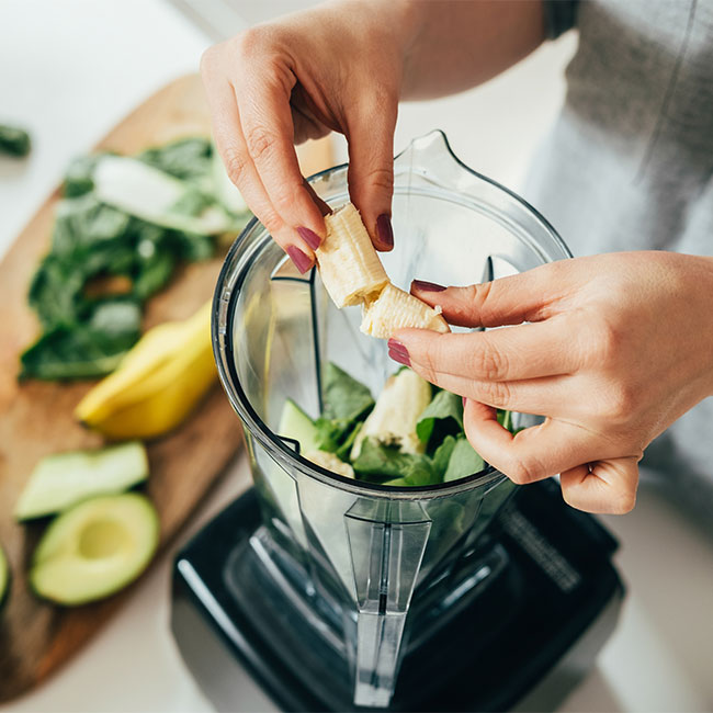 woman adding banana to smoothie in blender