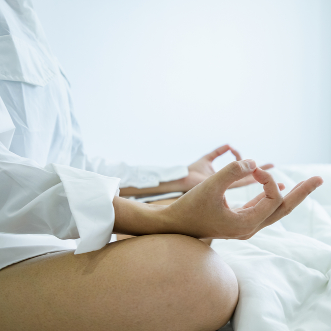 woman wearing white and meditating in bed with legs crossed