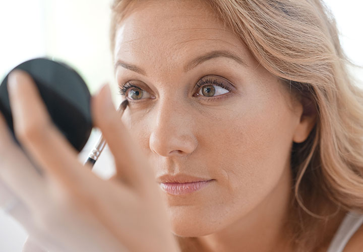 woman-applying-makeup-handheld-mirror