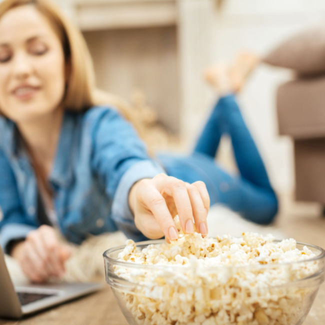 woman lying on stomach reaching for bowl of popcorn