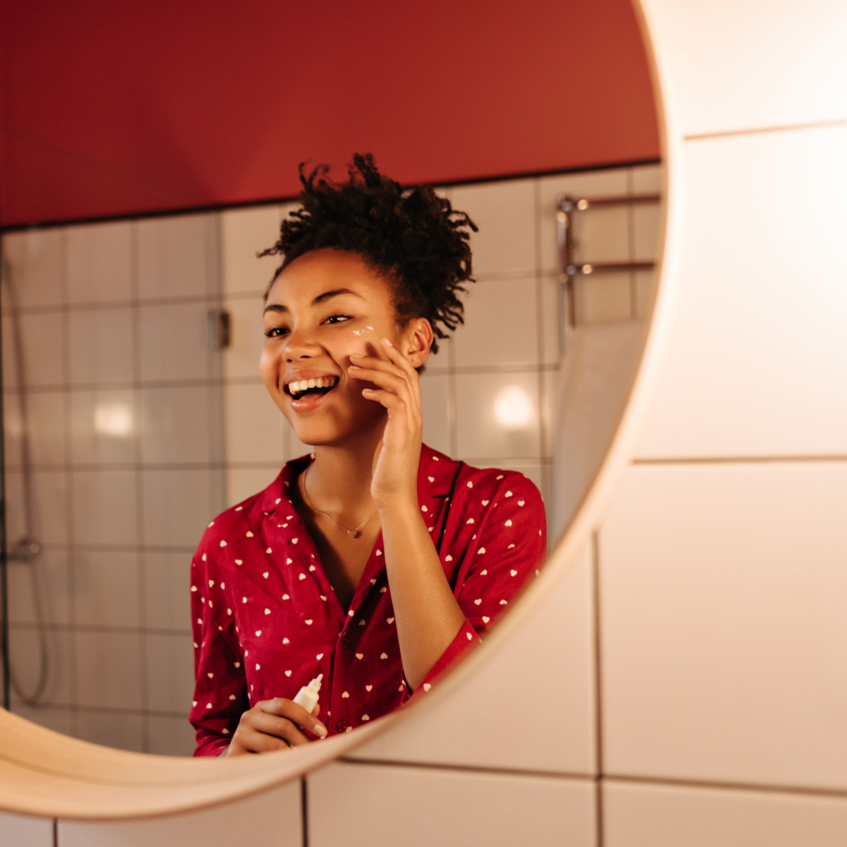 woman applying eye cream to under-eyes in warm light bathroom mirror