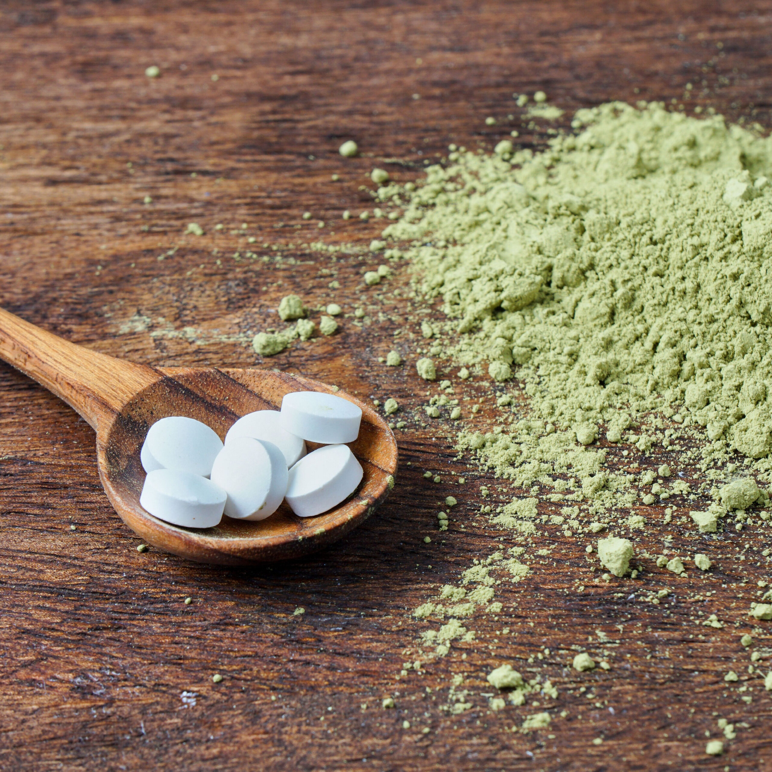 l-theanine supplements in wooden spoon beside green tea powder