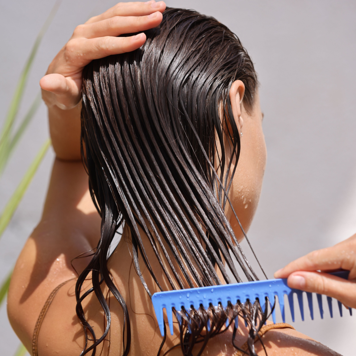 woman brushing through wet brown hair with a blue comb