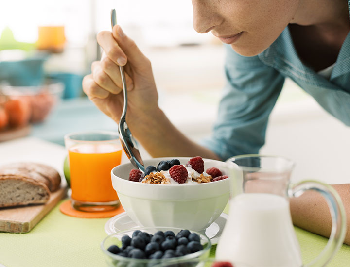 Woman eating a bowl of cereal with milk and fruit