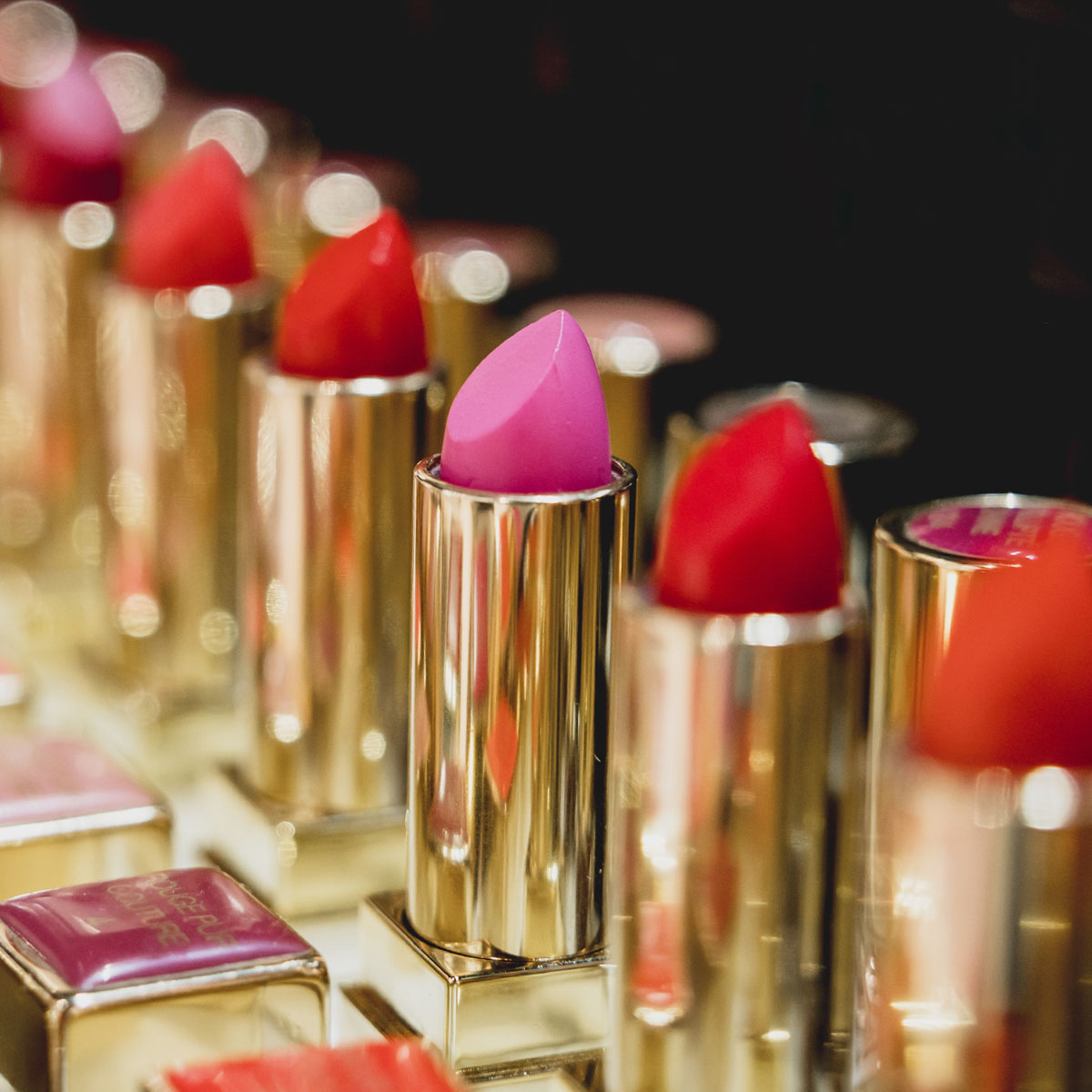 Geöffnete Tuben mit bunten Lippenstiften mit goldener Verpackung, die in einer Reihe von Make-up-Kosmetika sitzen