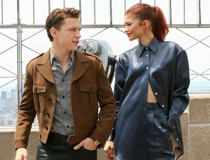 tom holland brown jacket blue top jeans zendaya red hair ponytail blue top unbuttoned nyc empire state building roof