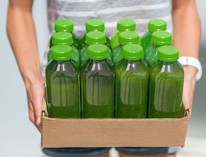 Person holding bottles of green juice from a cleanse fad diet