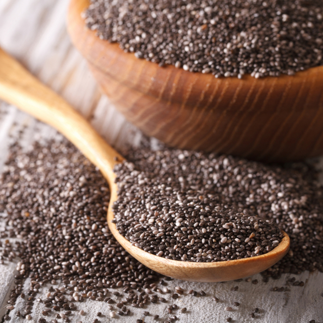 spoonful of chia seeds beside wooden bowl filled with them