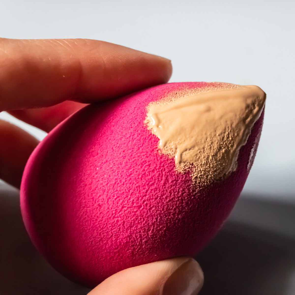 pink makeup sponge with concealer product on it dabbed finger holding cosmetic product