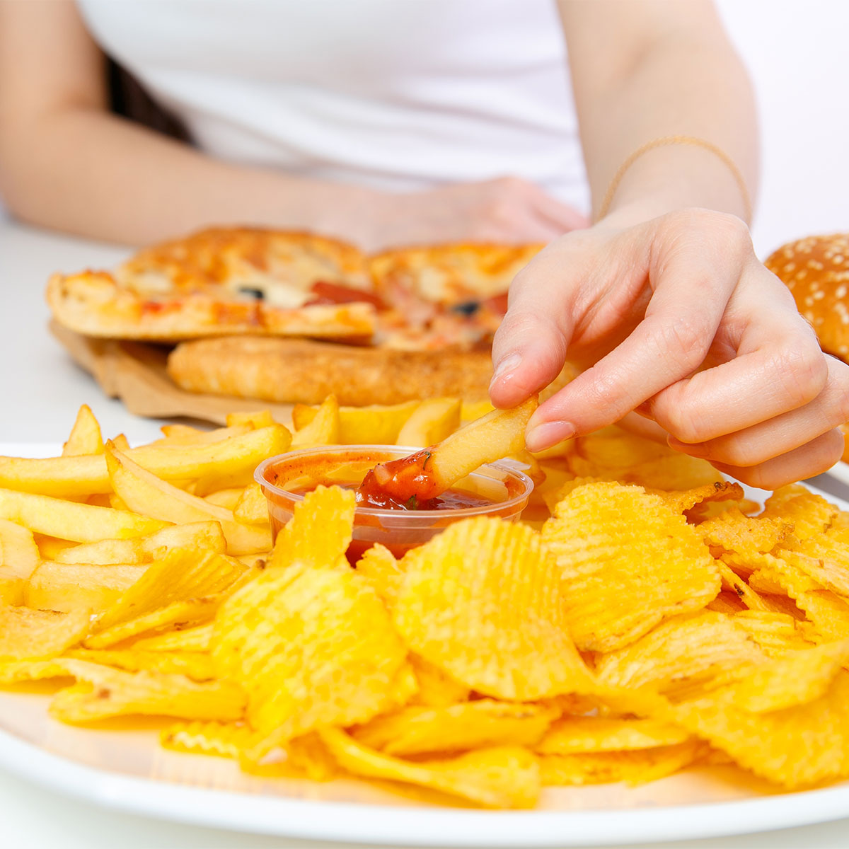 woman eating greasy yellow unhealthy potato chip snacks white plate white shirt