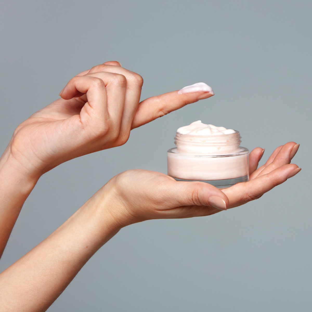 dipping finger into white lotion moisturizer product gray background isolated