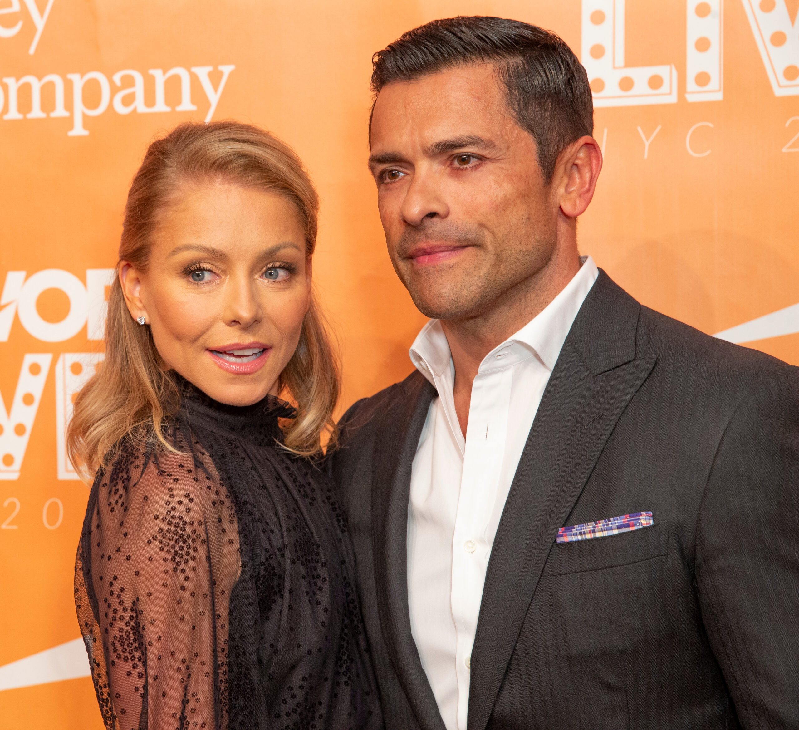 kelly ripa black dress mark consuelos black and white suit orange background red carpet