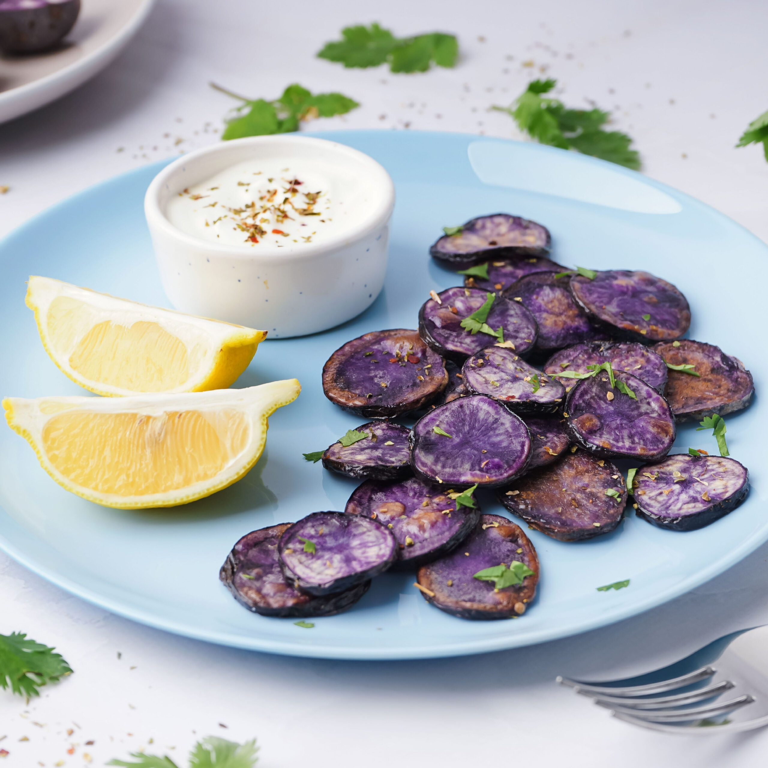 sliced purple potatoes on plate beside lemon wedges and dipping sauce