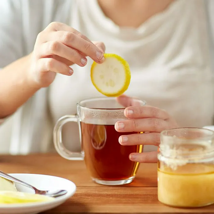 woman adding slice of lemon to cup of tea