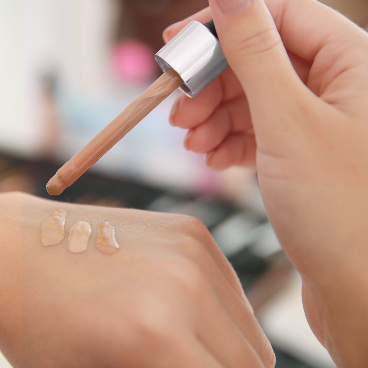 woman testing concealer swatches on hand with wand applicator store