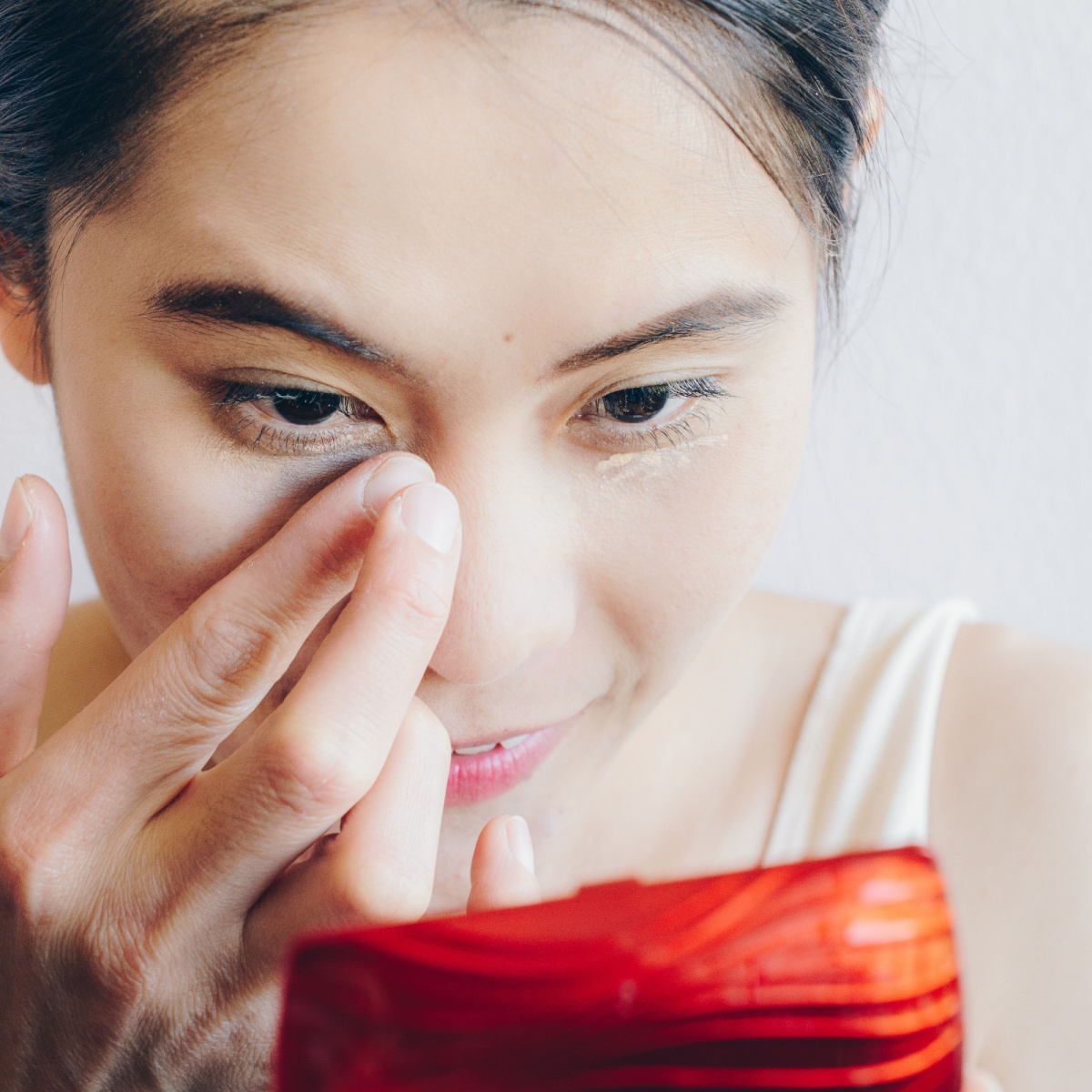 woman applying concealer makeup sponge under-eyes looking into compact mirror