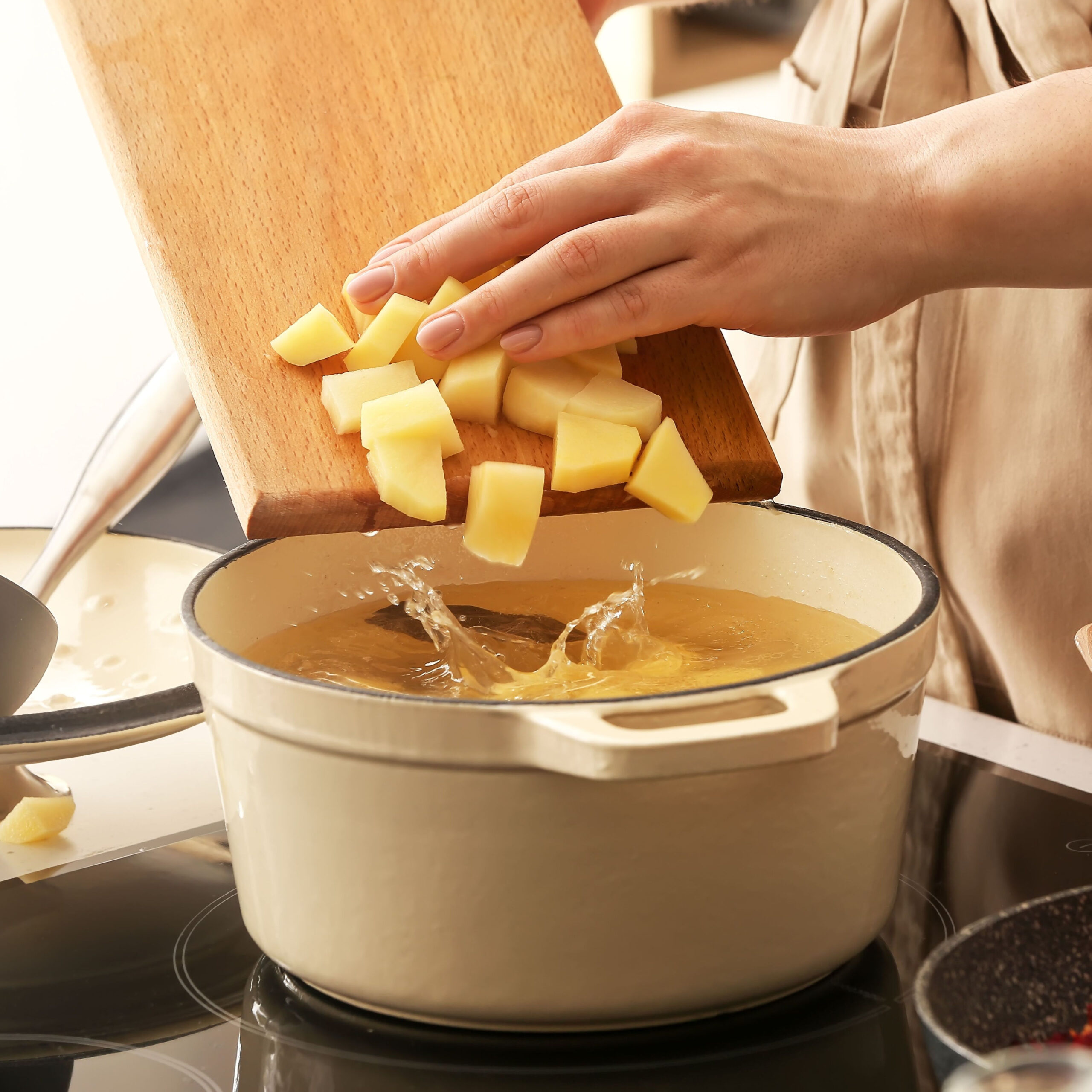 woman adding dice potatoes from cutting board to pot on stove