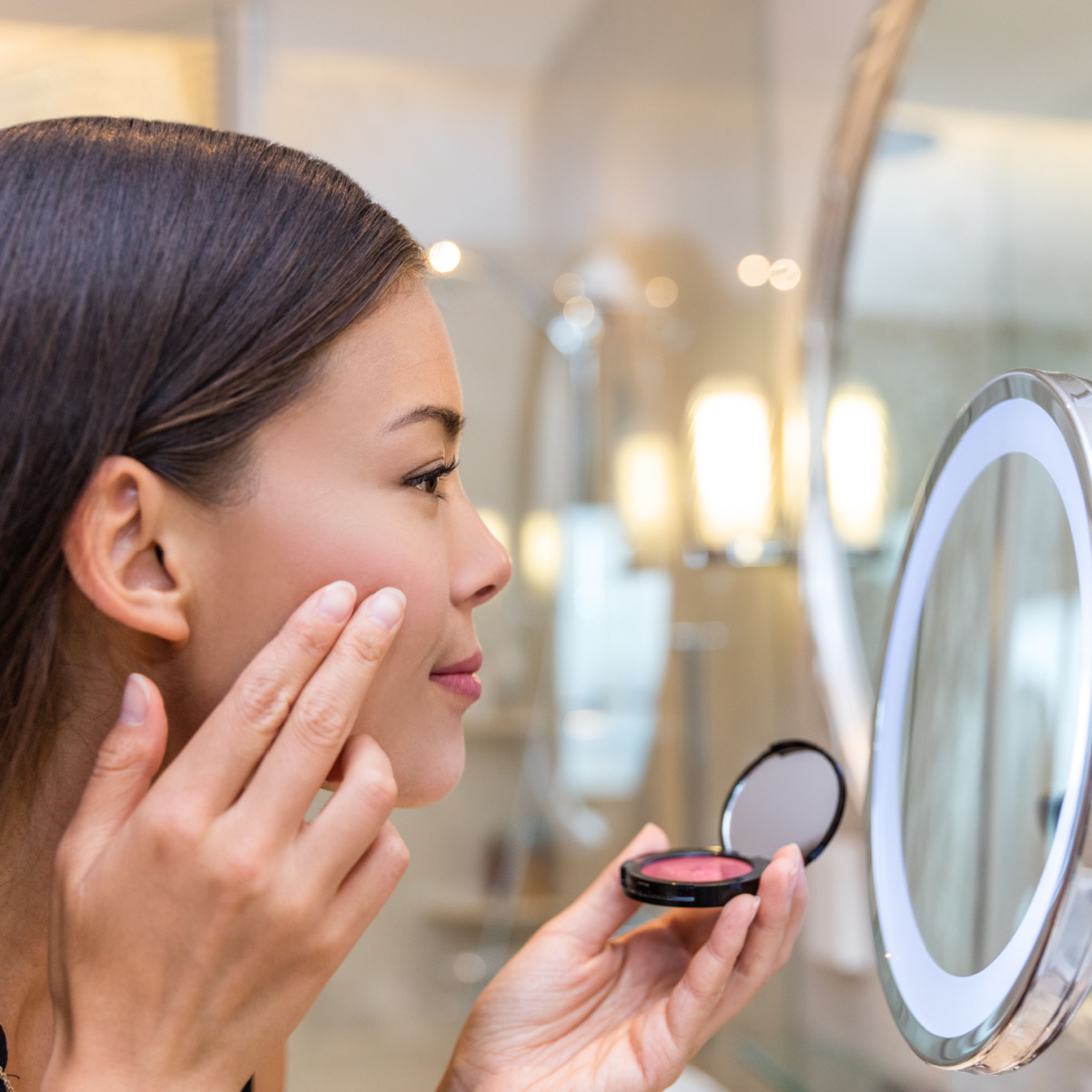 woman applying blush with finger mirror to cheekbone compact cosmetic product