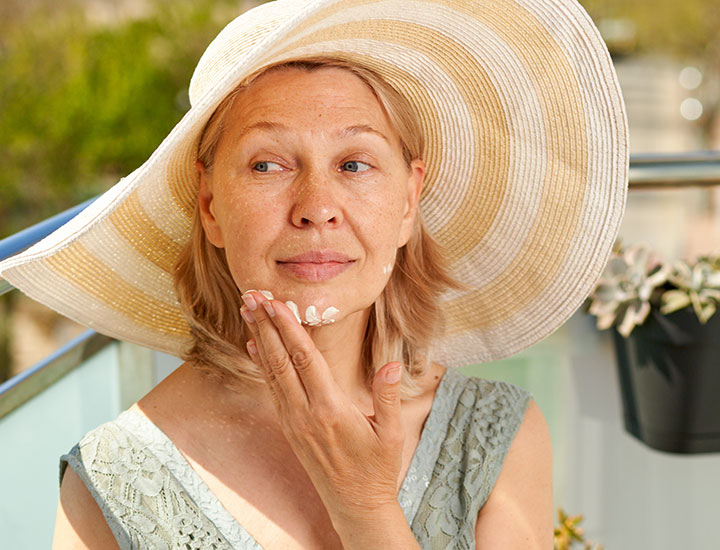 Ältere Frau, die ihr Gesicht mit Sonnencreme eincremt