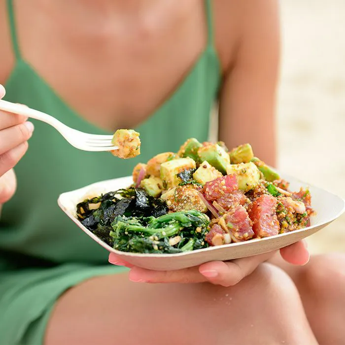 woman eating poke bowl salad at beach