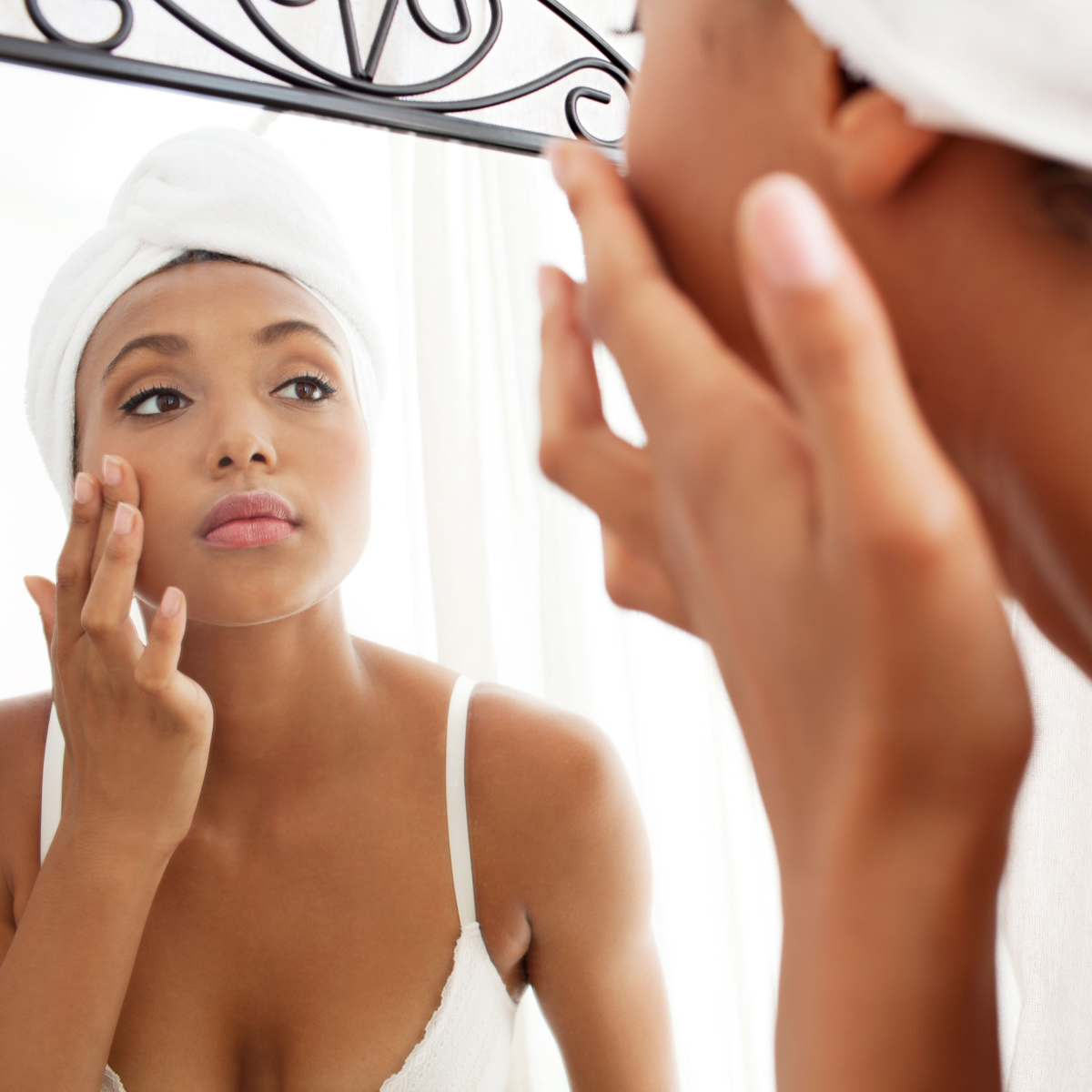woman looking into mirror touching skin white towel