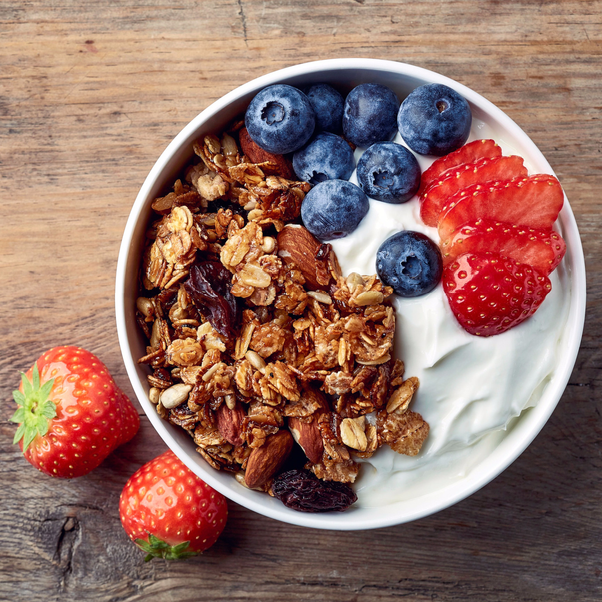 bowl of greek yogurt with oats blueberries strawberries wooden table white bowl breakfast