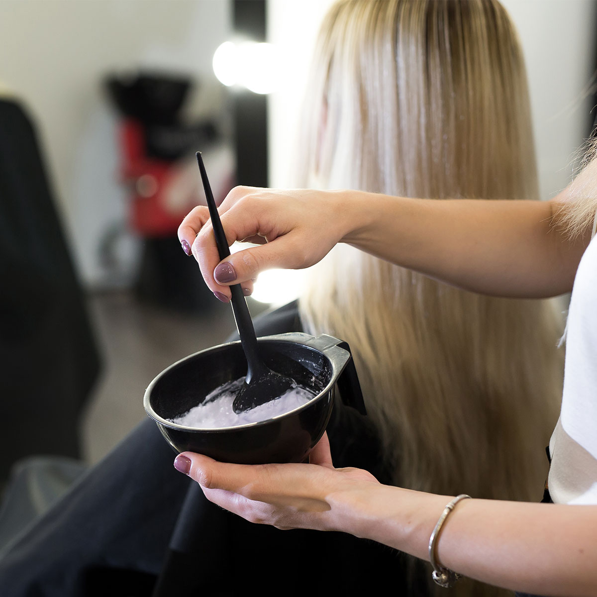 stylist mixing hair dye in salon black bowl blonde client