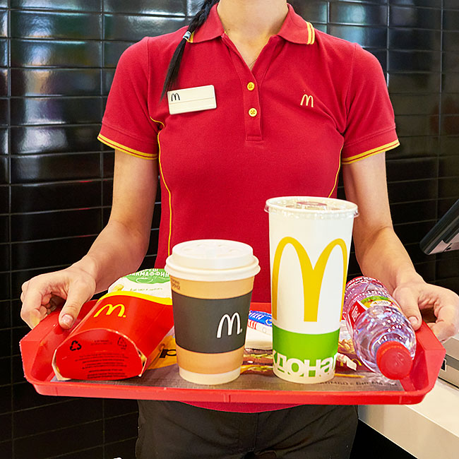 mcdonalds employee holding tray with burgers, fries, drink, and coffee