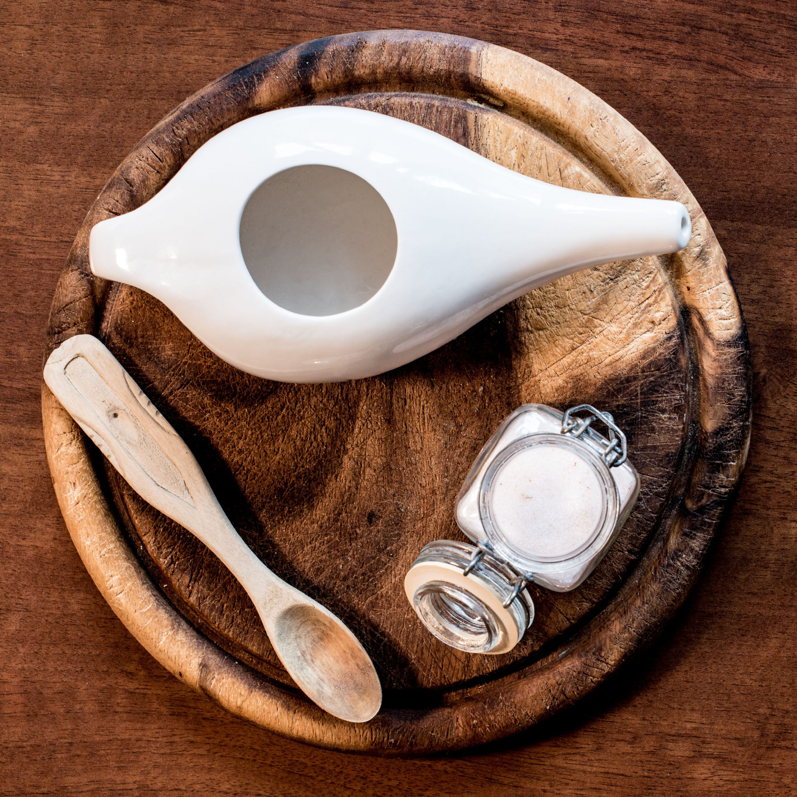 neti pot on wooden tray with small jar of salt and wooden spoon