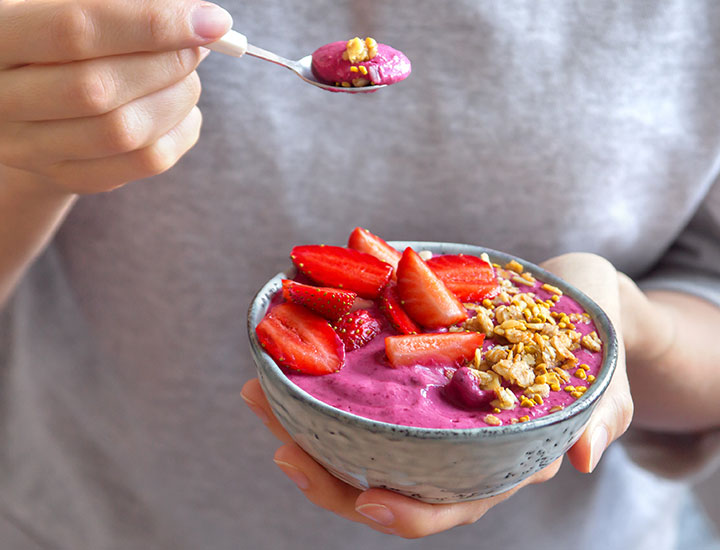 Person eating a pink smoothie bowl