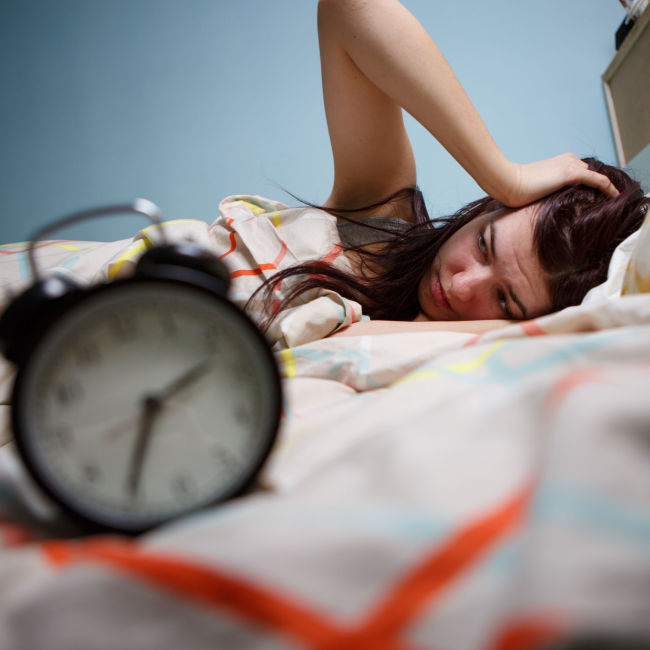 woman struggling to sleep in bed with alarm clock in foreground