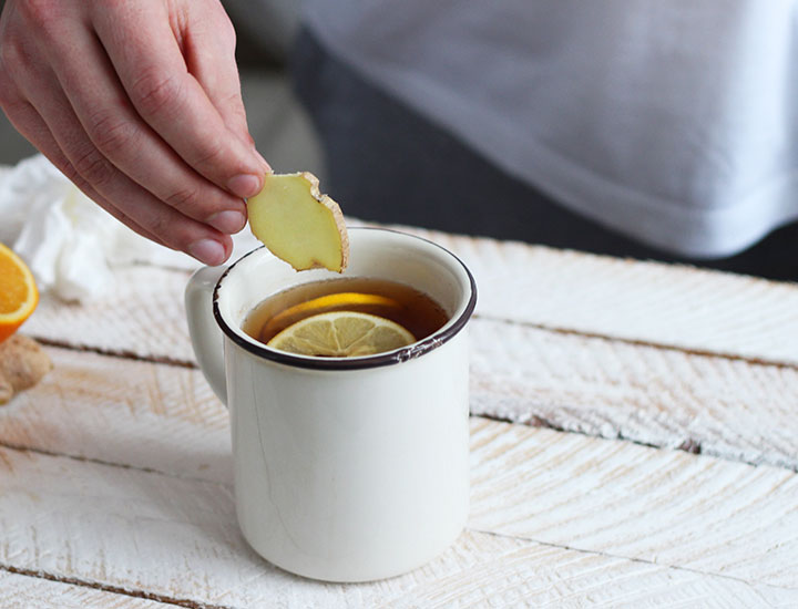 Person putting a ginger slice in tea