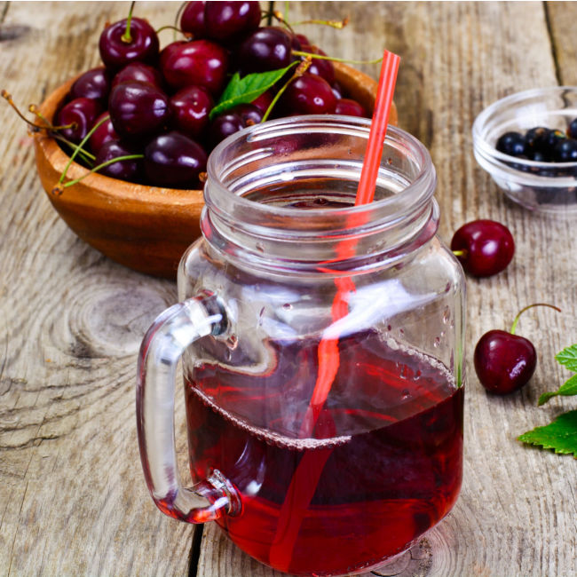 tart cherry juice in mason jar with handle beside small bowl of cherries