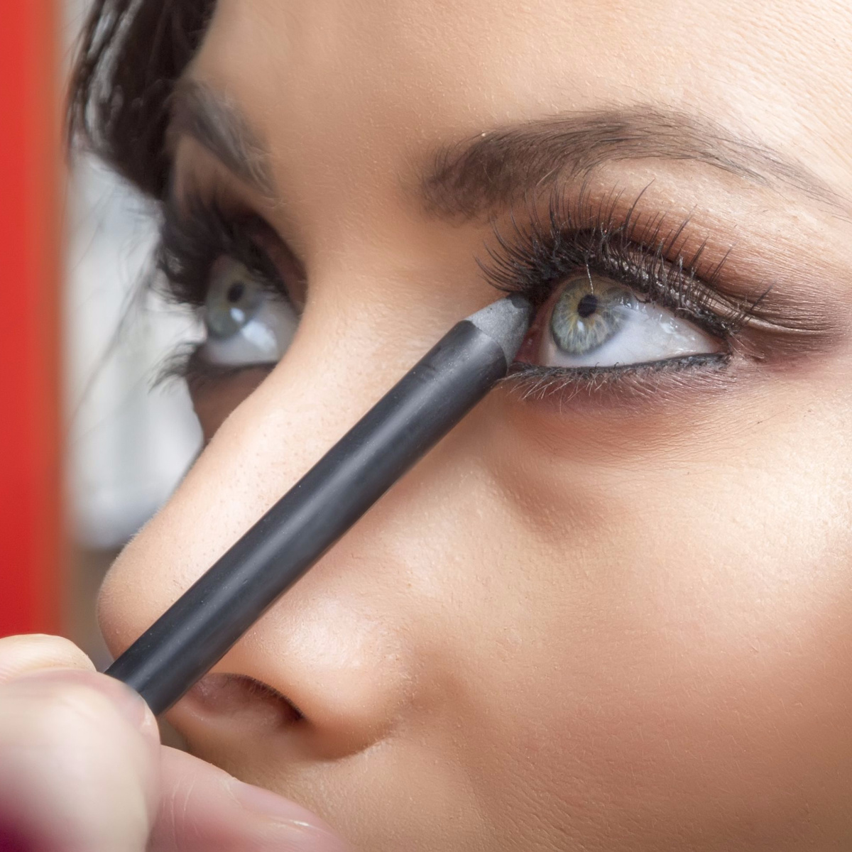 woman applying gray eyeliner pencil to waterline