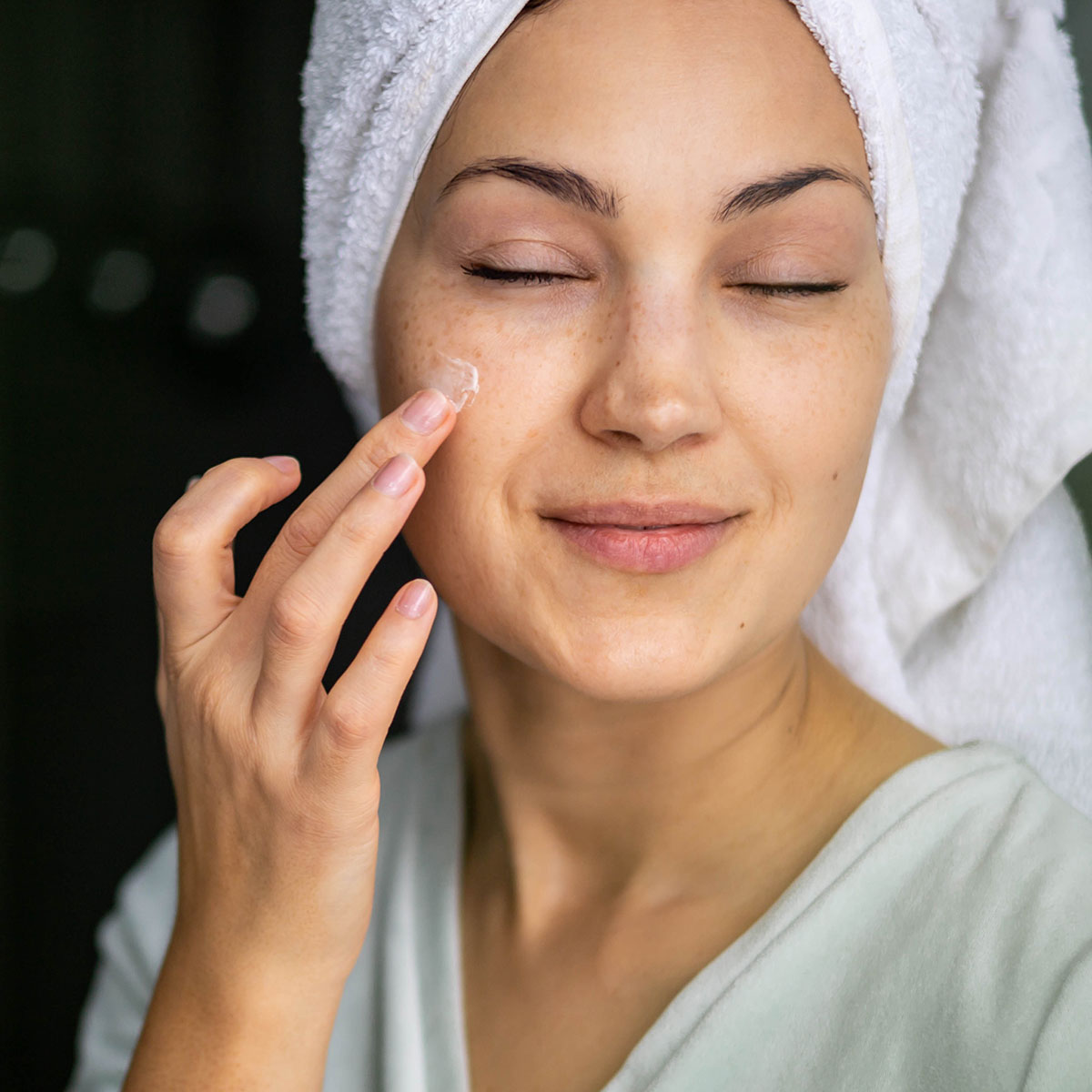 woman with white turban towel out of shower applying sunscreen with fingers to bare face