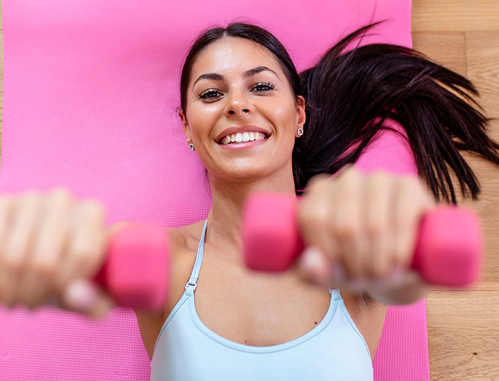 Woman lifting weight on a pink yoga mat