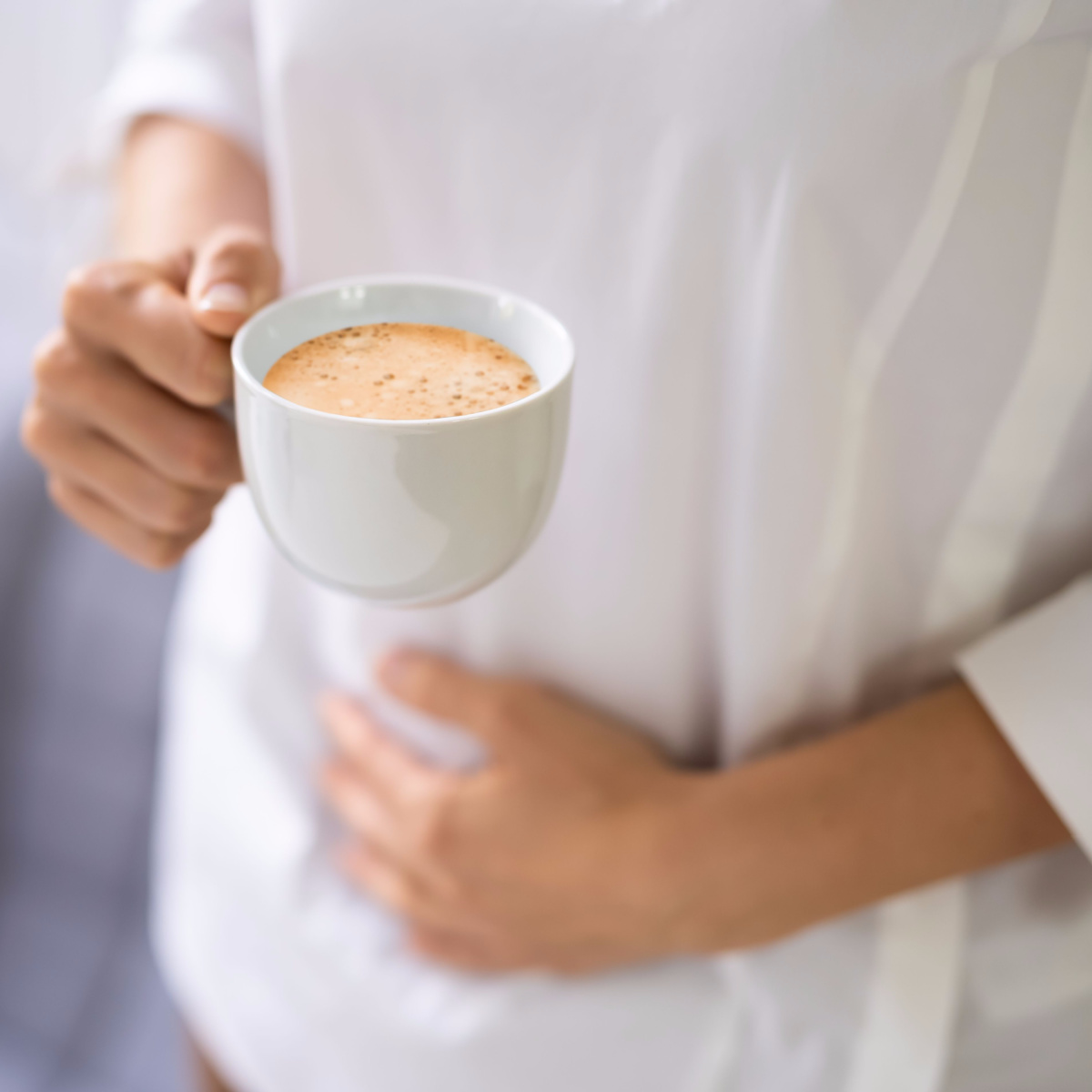 coffee bloating woman holding stomach cup of coffee