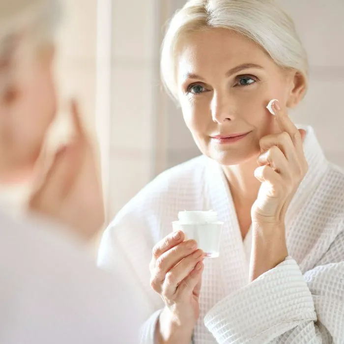 older mature woman applying sunscreen bathroom mirror robe